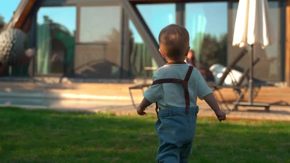 Toddler Walks Towards Mother with Ball Sitting on Chair