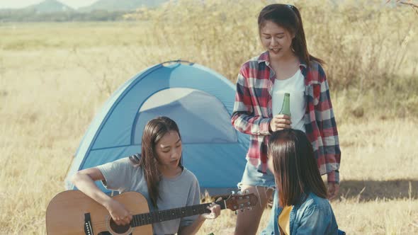 Asian woman happy camping in nature having fun together playing guitar and drinking beer.