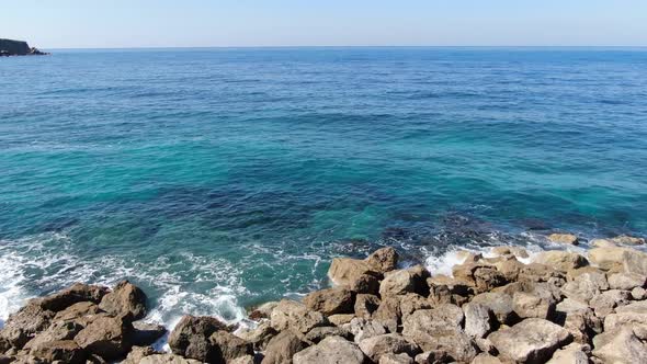 Camera Moves Forward From Rocky Coast Along Turquoise Blue Waves Rolling in Sunshine. Seascape of