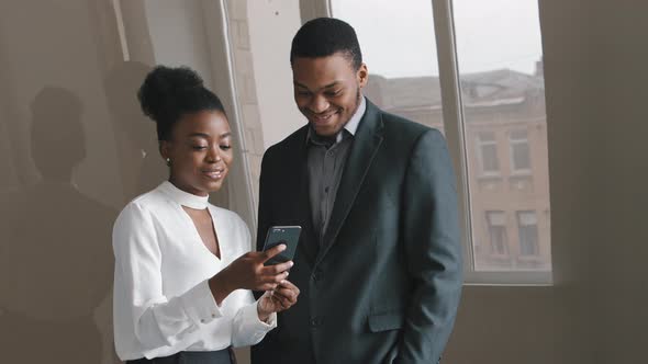 Happy Diverse Colleagues Talk Laugh Looking at Smartphone Using Funny Apps Standing in Office