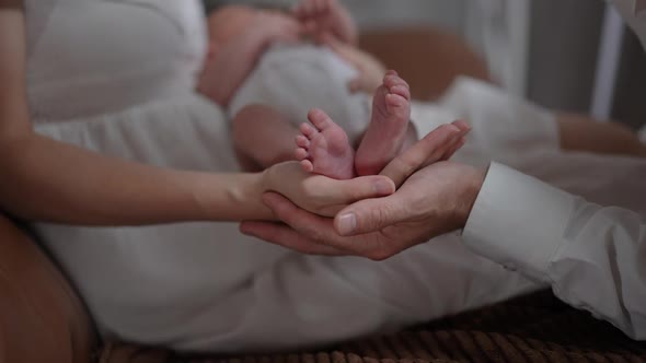 Closeup Tiny Newborn Baby Feet in Female Hand with Happy Man Kissing Little Toes in Slow Motion