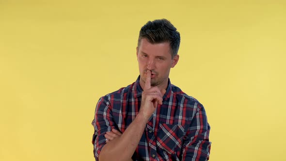 Close Up of Young Man Making a Hush Gesture on Yellow Background.