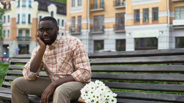 Sad African Man Sitting Lonely on City Bench With Flower Bouquet, Failed Date