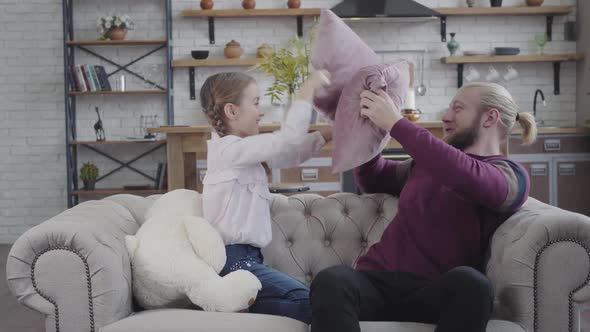 Joyful Caucasian Father and Daughter Sitting on Couch and Fighting with Pillows, Cheerful Man