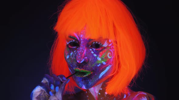 Portrait of Girl with Fluorescent Makeup and a Bright Orange Wig with a Lollipop
