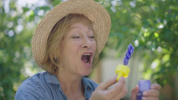 Closeup Laughing Senior Woman Blowing Soap Bubbles in Slow Motion Having Fun on Sunny Summer Spring