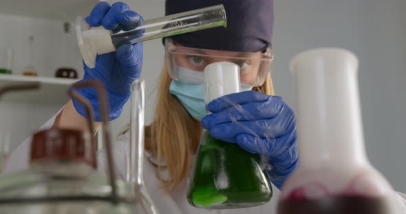 A Lab Worker Is Mixing Components in a Flask and Observing Their Reaction. On a Front Plan Flask