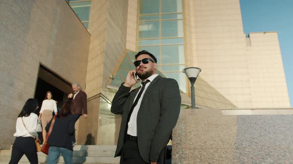 Joyful Businessman Enjoying Corporate Conversation on Mobile Phone Standing Near Office Center