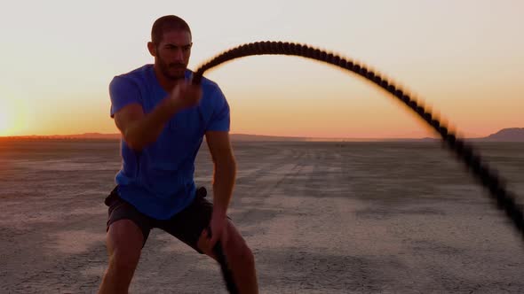 Athletic man working out with battle ropes on a dry lake at sunset