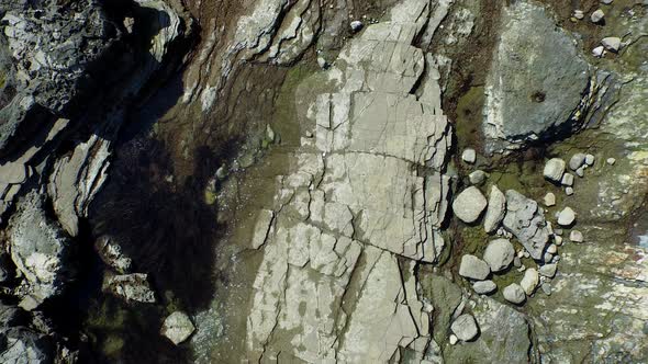 Aerial birds eye view shot of a young man running on a rocky ocean beach shoreline.