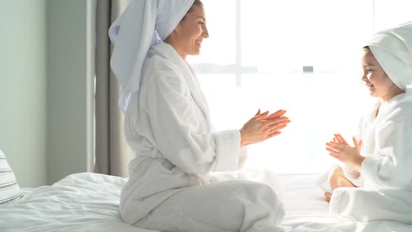 Young Pretty Mother and Daughter Dressed in a Dressing Gown Have Fun in Self-isolation Playing Hands