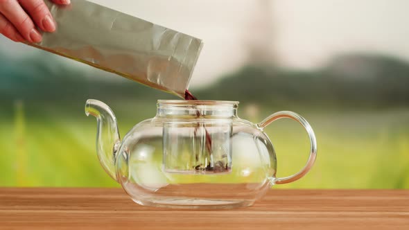 Putting Dry Tea Leaves Into Teapot on a Wooden Table