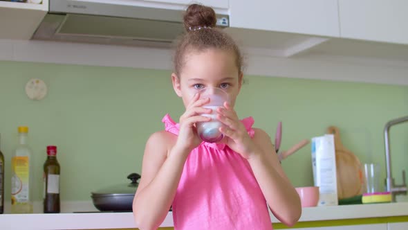 Cute Little Girl Drinking a Glass of Milk in the Kitchen at Home