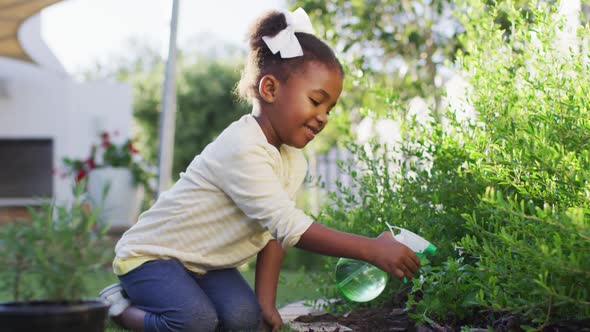 Happy african amercian girl gardening, watering plants in garden