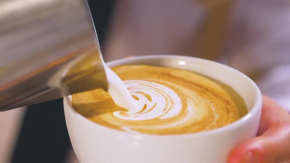 Person pouring milk into cup of coffee