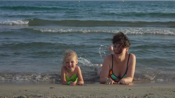 Mom and Daughter Are Laying on the Stomach Close Together on the Seashore