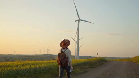 Young hiker with a camera walking near a farm with alternative green energy windmills