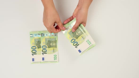 two female hands count one hundred euro paper bills on a white background