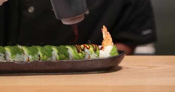 Skilled Chef Putting Sauce On Top Of Sushi Rolls Before Serving. Japanese Cuisine.  - close up shot