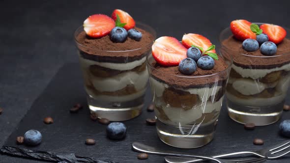 Classic Tiramisu Dessert with Blueberries and Strawberries in a Glass on Dark Concrete