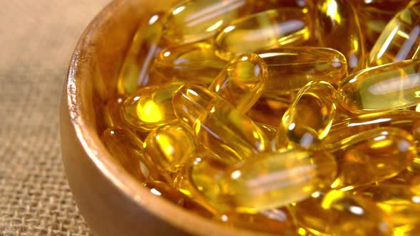 Fish oil capsules in rustic wooden bowl. Golden O???? 3 supplement pills. Macro