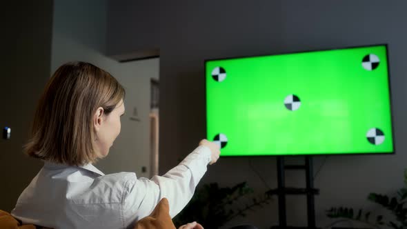 A girl is sitting at home in the living room and watching TV with a green screen Chroma Key