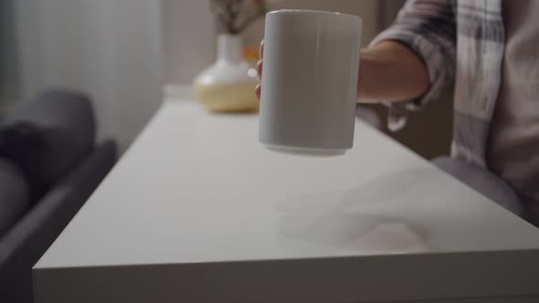 Female Hand Putting White Mug with Drink on Kitchen Counter Indoors