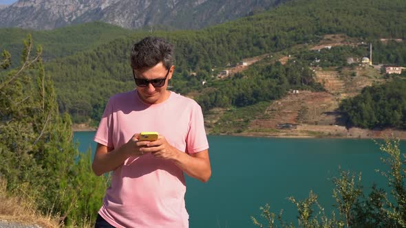 Man Texting Online on Mobile Phone of Mountains Lake Background