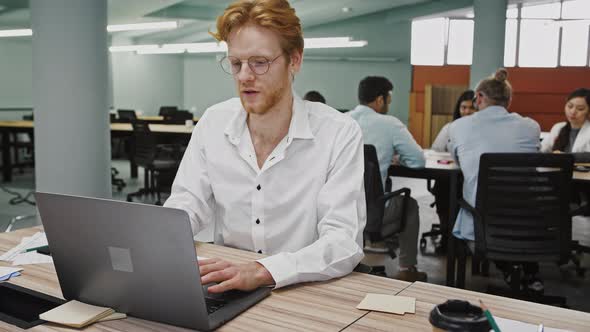 Young Man Working at Notebook Sitting at Table in Office Made a Good Deal Leaning Back in Chair and