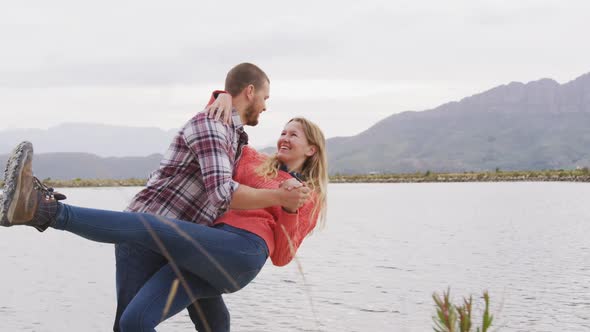 Caucasian couple having a good time on a trip to the mountains, dancing near lake and smiling