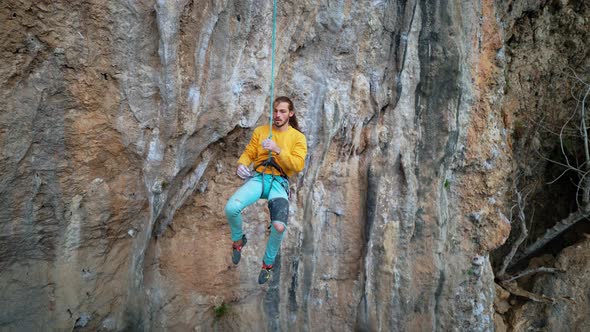 Slow Motion of Joyful Handsome Man Rock Climber in Yellow Sweatshirt with Long Hair Hanging on Rope