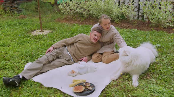 A Young Couple, a Guy and a Girl in the Family Garden on the Grass Playing with a Samoyed Dog.