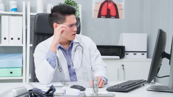 Stressed and overworked Asian male doctor sitting on table in hospital.