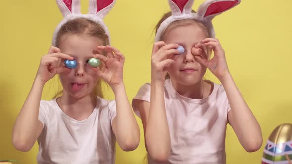 Cute Sisters with Bunny Ears Keeping Colorful Quail Eggs Near Eyes and Showing Tongues While