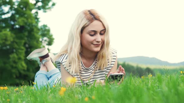 Young European Girl Lying on the Grass and Typing in Her Phone