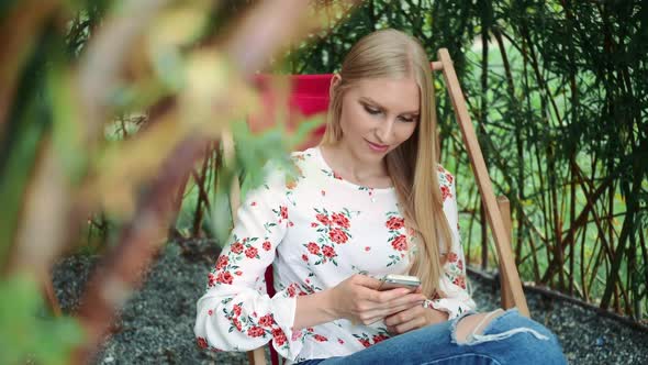Young Woman Using Smartphone in Plant Gazebo