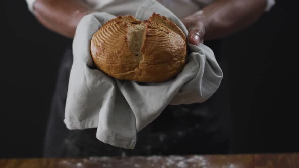 Video of cook holding loaf of bread on black background