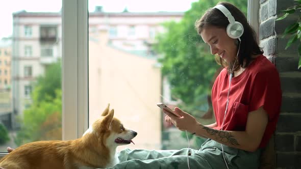 Hipster Millennial Young Woman Listen to Music in Headphones and Stroke Corgi Dog Avki