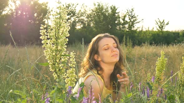 Pretty Young Girl is Sitting in the Middle of the Field with Flowers During Summer Time