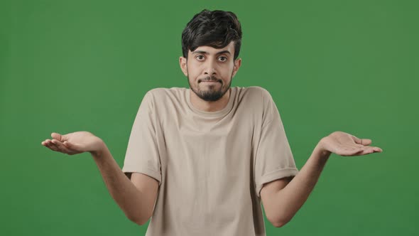 Portrait of Puzzled Uncertain Arabic 20s Guy Standing on Green Background Unsure Embarrassed