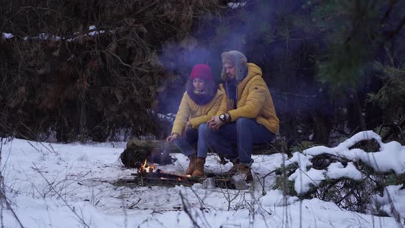 Young Man and Woman Near a Campfire in the Forest in Winter