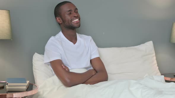 Happy Young African Man Sitting in Bed Thinking 