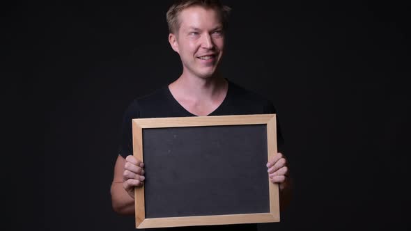 Young Handsome Man Holding Blackboard Against Black Background