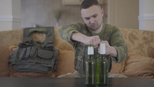 The Man in Military Closes Opening Beer Sitting at Home on the Sofa. Unhappy Man