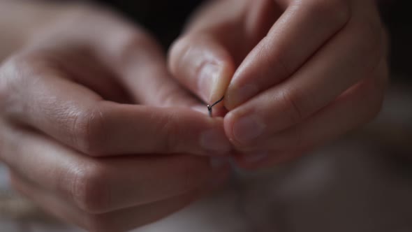 Close-up view of female hands inserting a thread into a needle hole for sewing. Handmade needlework.