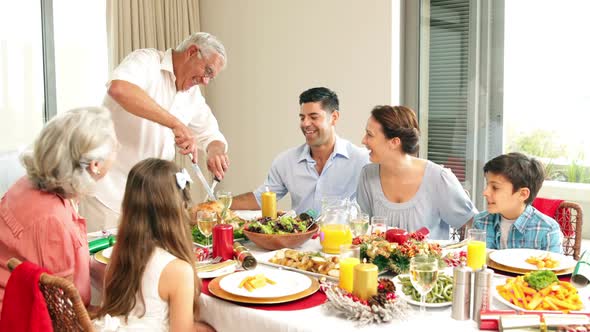 Grandfather carving chicken at dinner table for his family