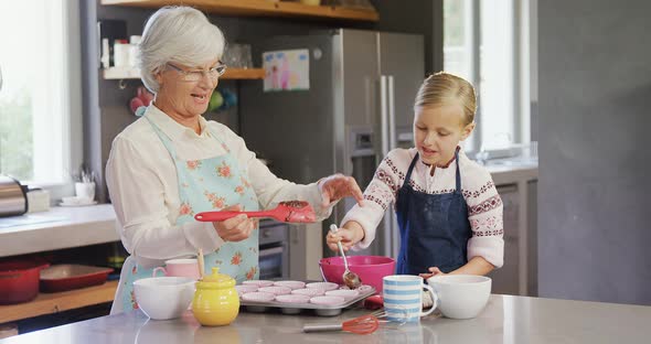 Happy grandmother and granddaughter filling cup cakes 4k