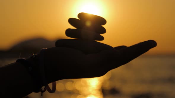 Silhouette of a Hand with Pebble Stones on a Background of Sunset and Sea. Balance Concept.