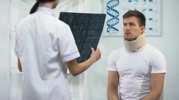 Female Surgeon Informing Patient in Foam Cervical Collar About Bad X-Ray Result