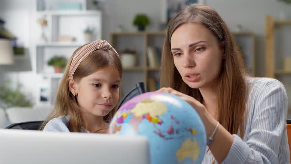 Mom and Daughter Study Geography Using the Globe at Home at the Desk